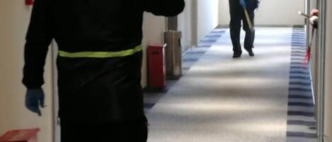 Un pasillo con alfombra estampada, puertas a la derecha y una persona alejándose de la cámara.