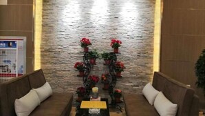 Un hall d’entrée avec un mur en pierre, deux canapés avec des coussins, une table basse avec un menu et des plantes en pot.