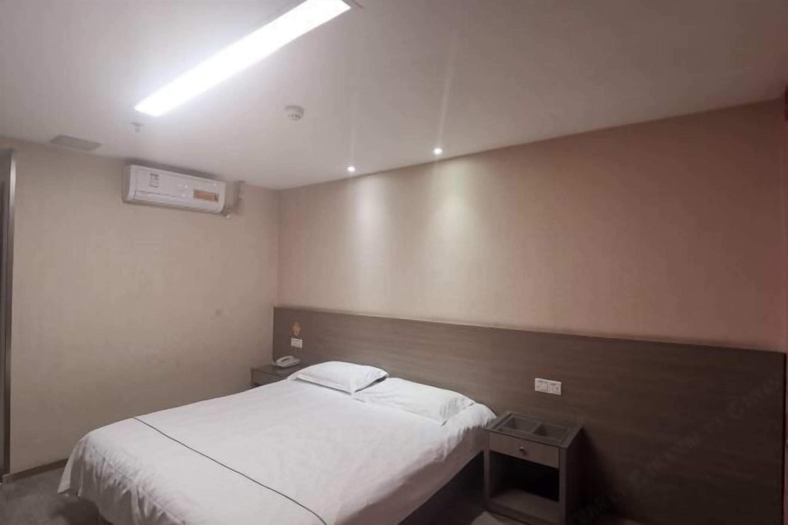 A hotel room with a bed, bedside table, and a wall-mounted air conditioning unit.