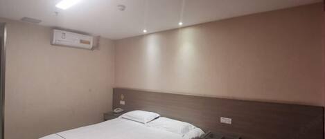 A hotel room with a bed, bedside table, and a wall-mounted air conditioning unit.