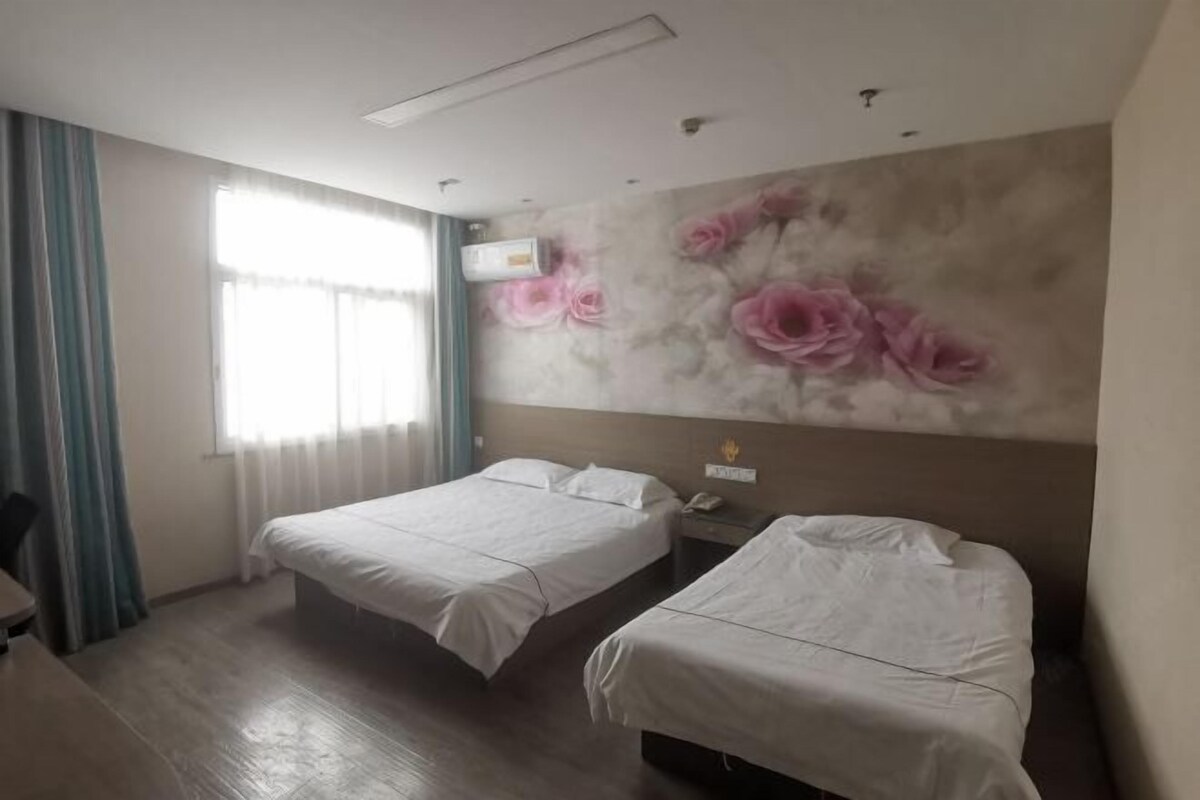 Une chambre d’hôtel avec deux lits, un bureau, une chaise, une fenêtre avec des rideaux et un mur orné d’une fresque florale.