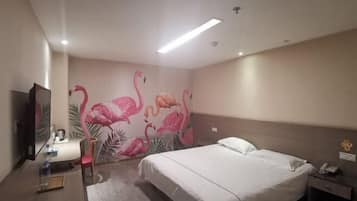A hotel room with a bed, a nightstand, a desk with a lamp, a mirror, and a wall with a flamingo mural.