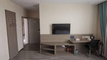 A hotel room with a flat-screen TV mounted on the wall, a wooden desk with a chair, and a small seating area.