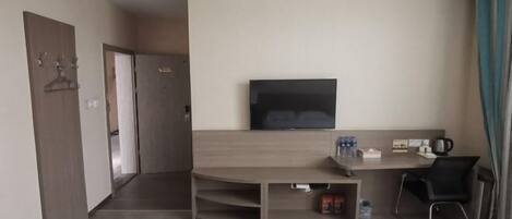 A hotel room with a flat-screen TV mounted on the wall, a wooden desk with a chair, and a small seating area.