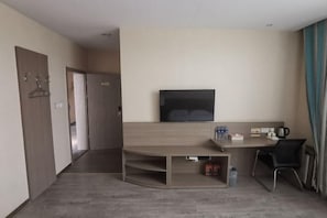 Ein Hotelzimmer mit flachbildfernseher an der Wand, einem Holztisch mit Stuhl und einer kleinen Sitzecke.