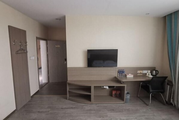 Une chambre d’hôtel dotée d’un téléviseur à écran plat fixé au mur, d’un bureau en bois avec une chaise et d’un petit coin salon.