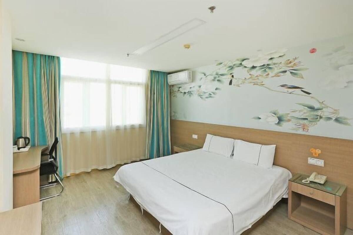Une chambre d’hôtel comprenant un lit, un bureau, une chaise, une table de chevet et un mur orné d’une fresque florale.