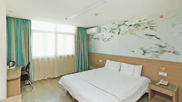 A hotel room with a bed, a desk, a chair, a nightstand, and a wall with a floral mural.
