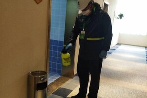 A person in a dark uniform spraying a yellow bottle on a metallic object. - Mingyue Business Hotel (Shijiazhuang)