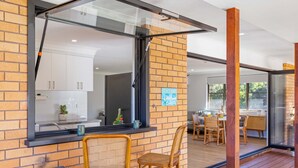 A modern kitchen with white cabinets and a brick wall. There is a window with a view of the outside. - Joeys Getaway North Haven (North Haven)