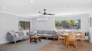 A modern living room with a grey sofa, wooden coffee table, and a dining area with a round table and chairs. - Joeys Getaway North Haven (North Haven)