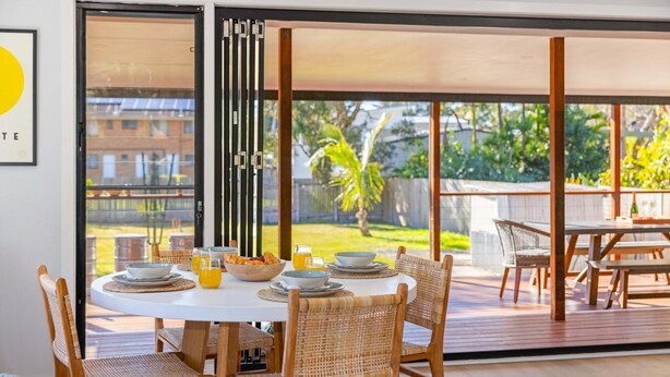 A dining area with a round table, wicker chairs, and a view of a garden through large sliding glass doors. - Joeys Getaway North Haven (North Haven)