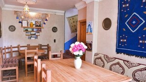 A wooden dining table with chairs, a vase of flowers, and a patterned wall tapestry. - A Secret Garden (Toudgha El Oulia)