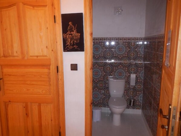 Un baño con puerta de madera, un inodoro y azulejos estampados.