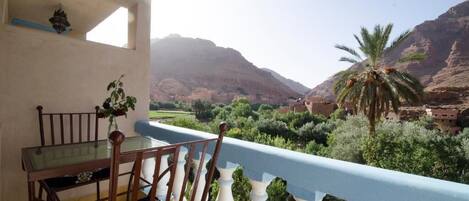 A balcony with a table and chairs, overlooking a mountainous landscape with greenery and a palm tree.