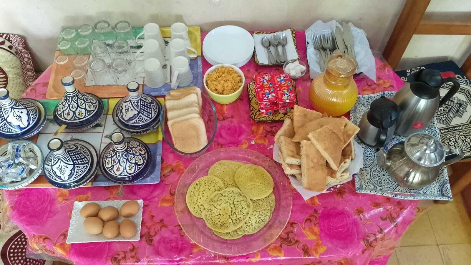 A table with various food items, utensils, and containers, likely set for a meal.