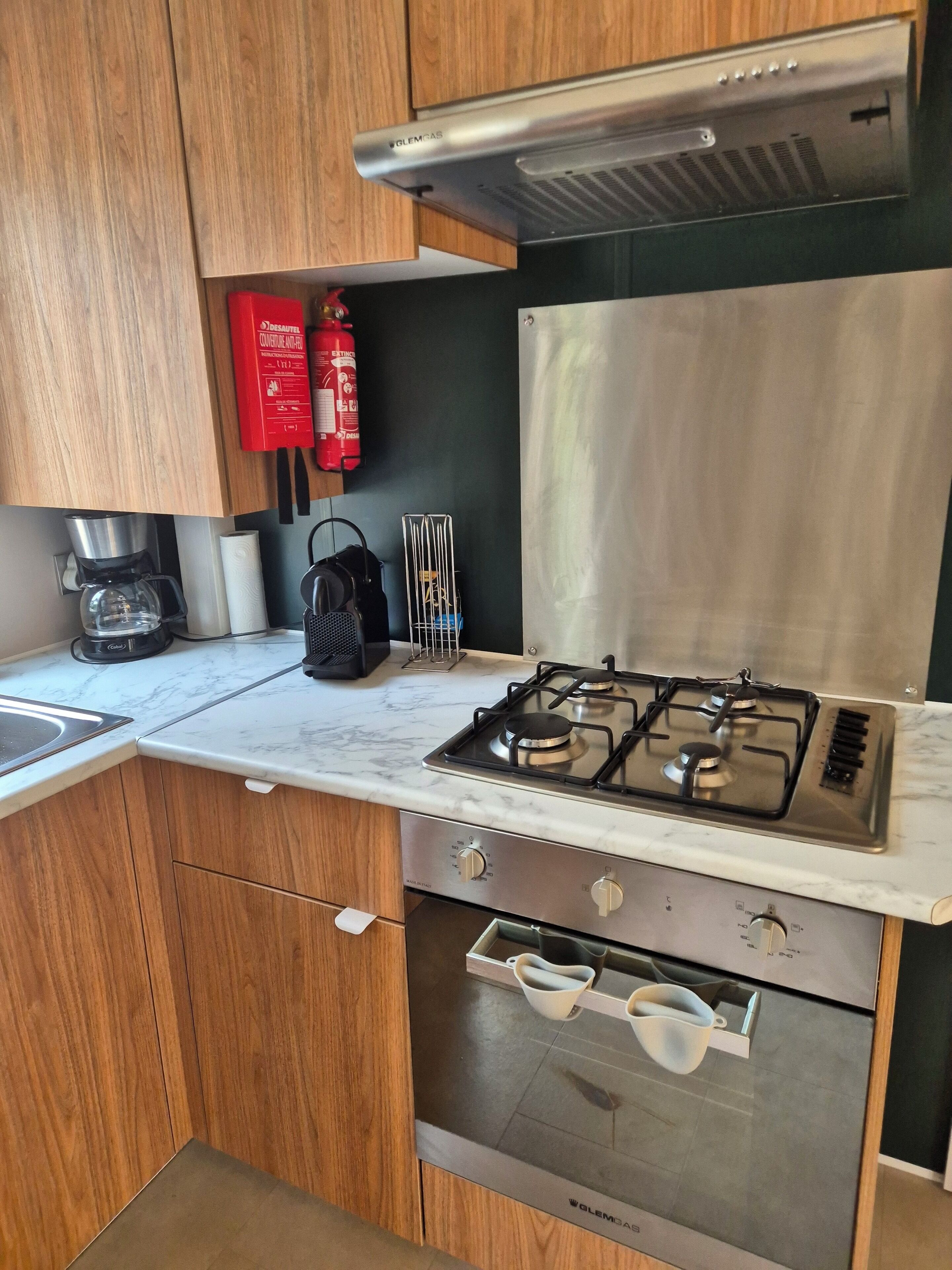 A modern kitchen with wooden cabinets, a stainless steel range hood, a gas stove, and a coffee maker.