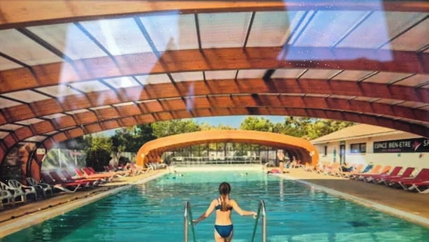 Une piscine intérieure dotée d’un toit abrité, d’une eau claire et de chaises longues disposées tout autour.