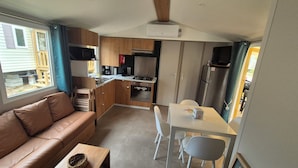 Une petite cuisine équipée avec une cuisinière, un four à micro-ondes et un réfrigérateur. Il y a un petit coin repas avec une table et des chaises. Un canapé en cuir marron se trouve dans l’espace salon.