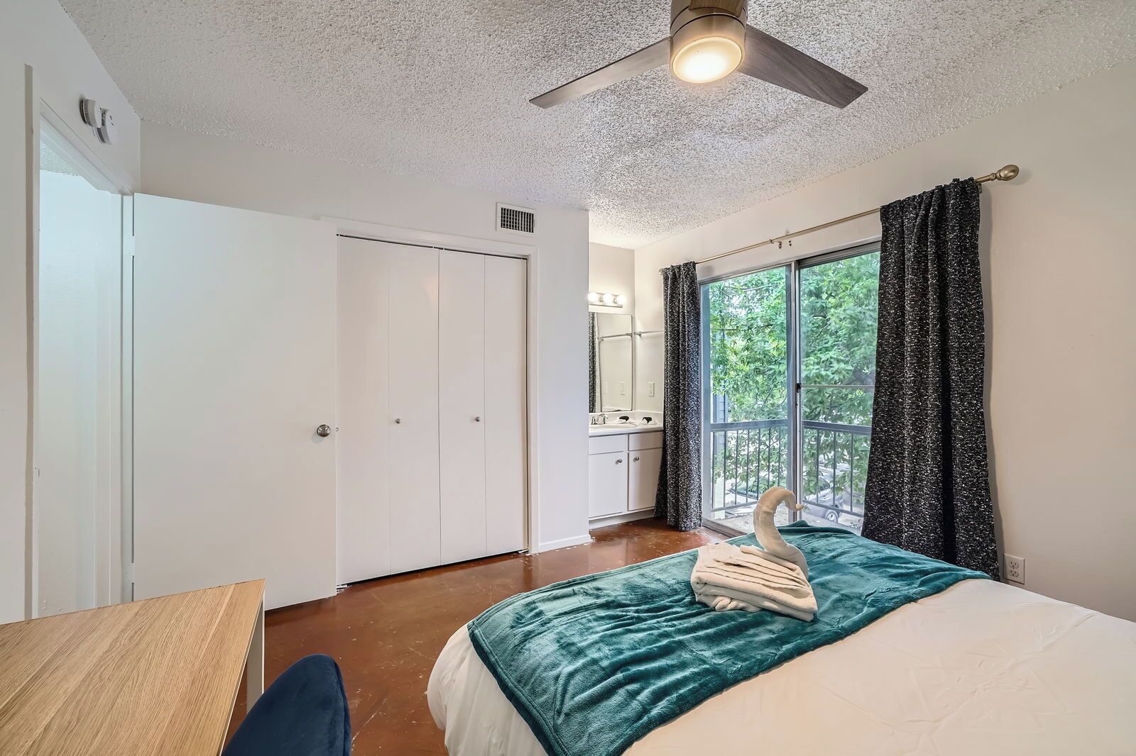 A bedroom with a bed, a desk, a ceiling fan, and a window with curtains.