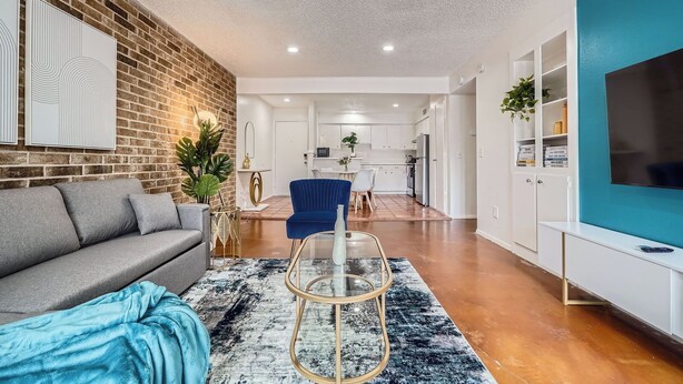 A modern living room with a grey sofa, a blue armchair, and a glass coffee table. - 2B Getaway | Steps 2 Dtwn | Sleeps 6 | Pool + Prkg (Austin)