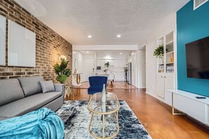 A modern living room with a grey sofa, a blue armchair, and a glass coffee table. - 2B Getaway | Steps 2 Dtwn | Sleeps 6 | Pool + Prkg (Austin)