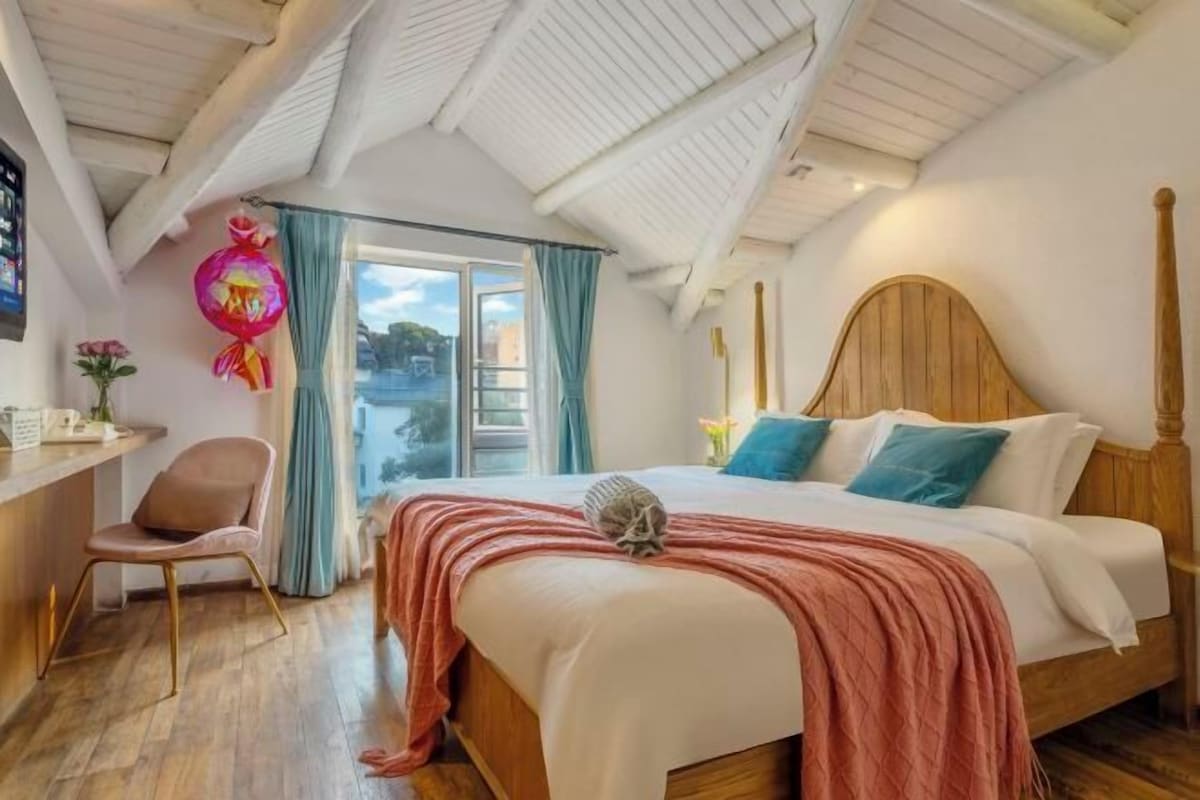 Une chambre à coucher avec un lit en bois, un bureau avec une chaise et une fenêtre avec des rideaux.