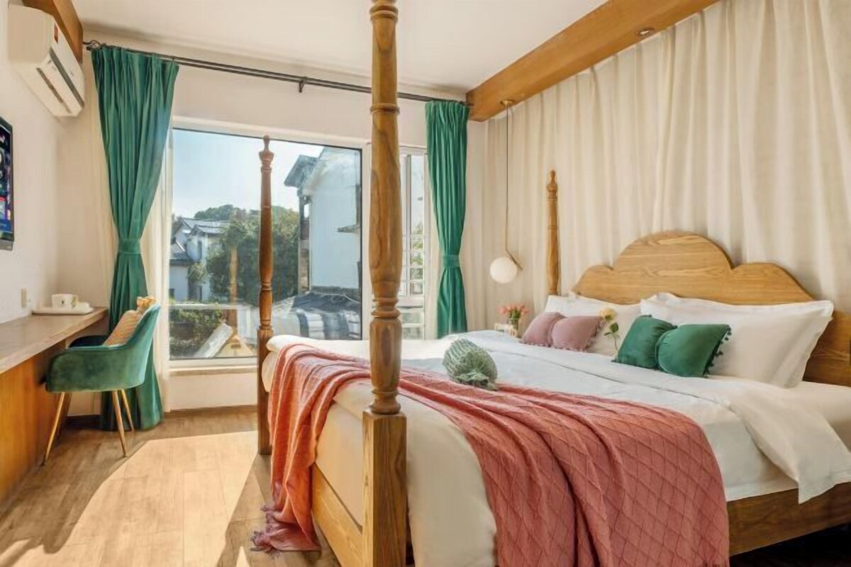 Une chambre à coucher avec un lit à baldaquin, un bureau avec une chaise et une grande fenêtre avec des rideaux.