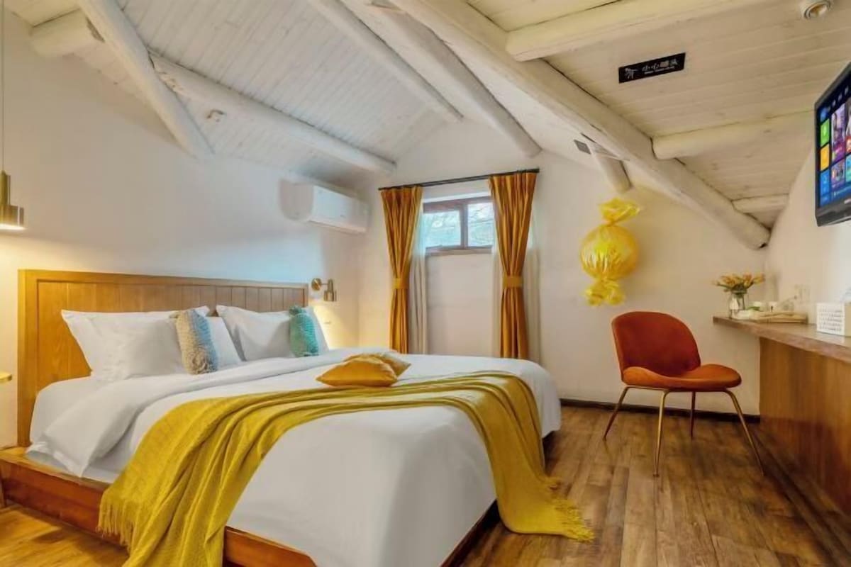 Une chambre d’hôtel avec un lit, une tête de lit en bois, un bureau avec une chaise et une fenêtre avec des rideaux.