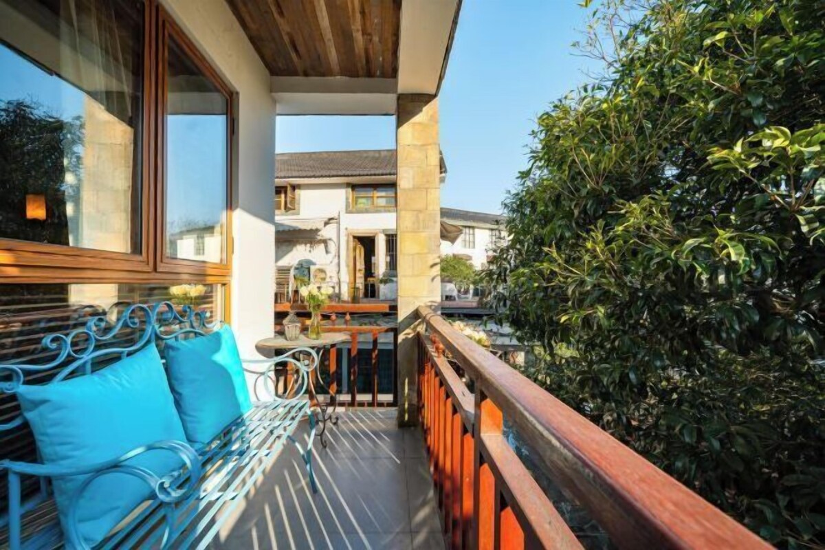 Un balcon avec un banc en métal, une balustrade en bois et une vue sur une maison au loin.