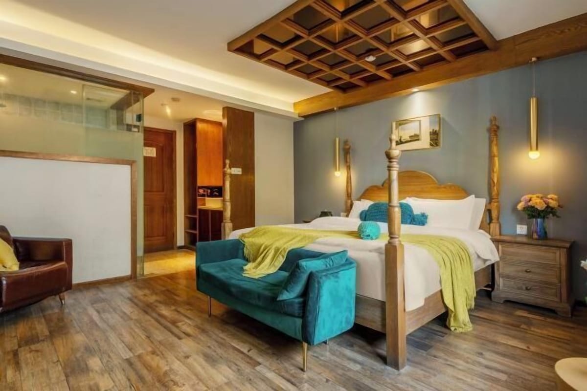 Une chambre à coucher avec un plafond en bois, un lit à baldaquin, un fauteuil vert et une table de chevet ornée d’un vase de fleurs.