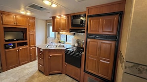 A compact RV kitchen with wooden cabinets, a stove, microwave, and a sink.