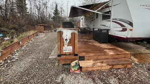 A recreational vehicle with a covered deck area, surrounded by a gravel path and wooden decking.