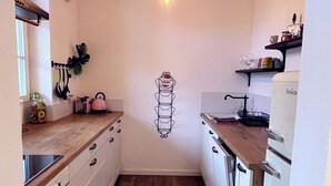 Een kleine keuken met witte kastjes, een houten aanrechtblad en een hanglamp.