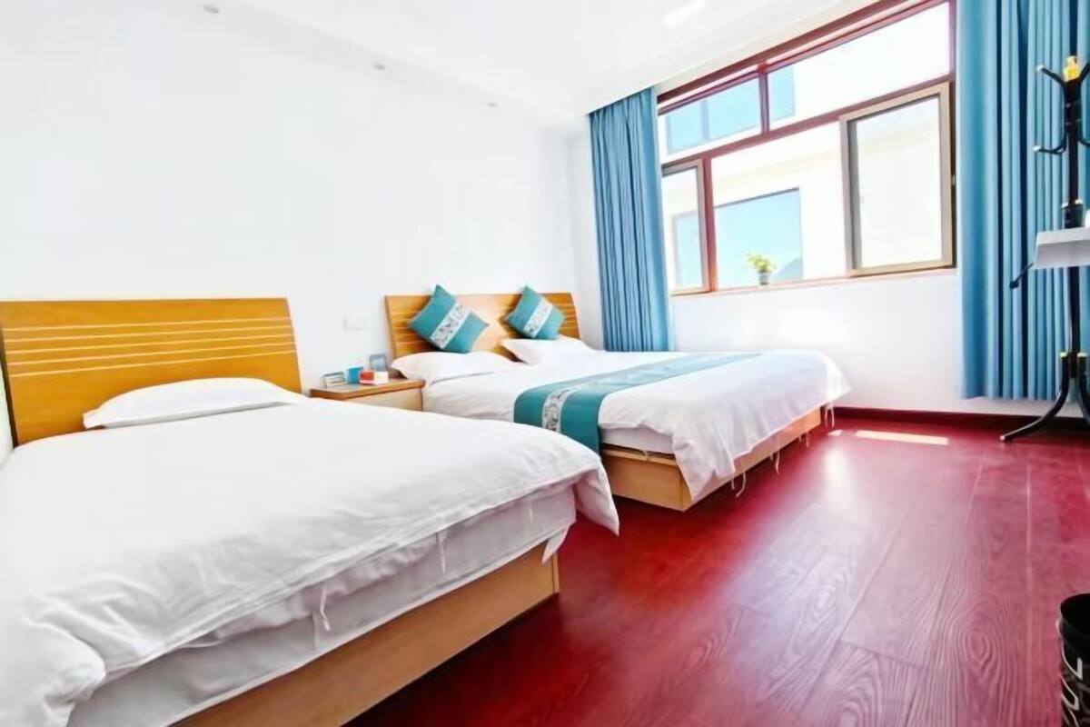 A hotel room with two beds, a wooden headboard, a window with curtains, and a red wooden floor.