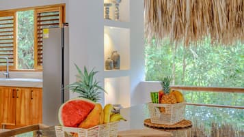 A modern kitchen with a glass-top island, wicker baskets with fruits, and a thatched ceiling.