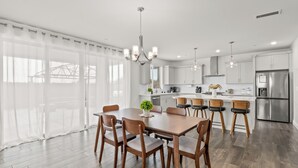 Una cocina moderna con armarios blancos, electrodomésticos de acero inoxidable y una zona de comedor con sillas y mesa de madera.