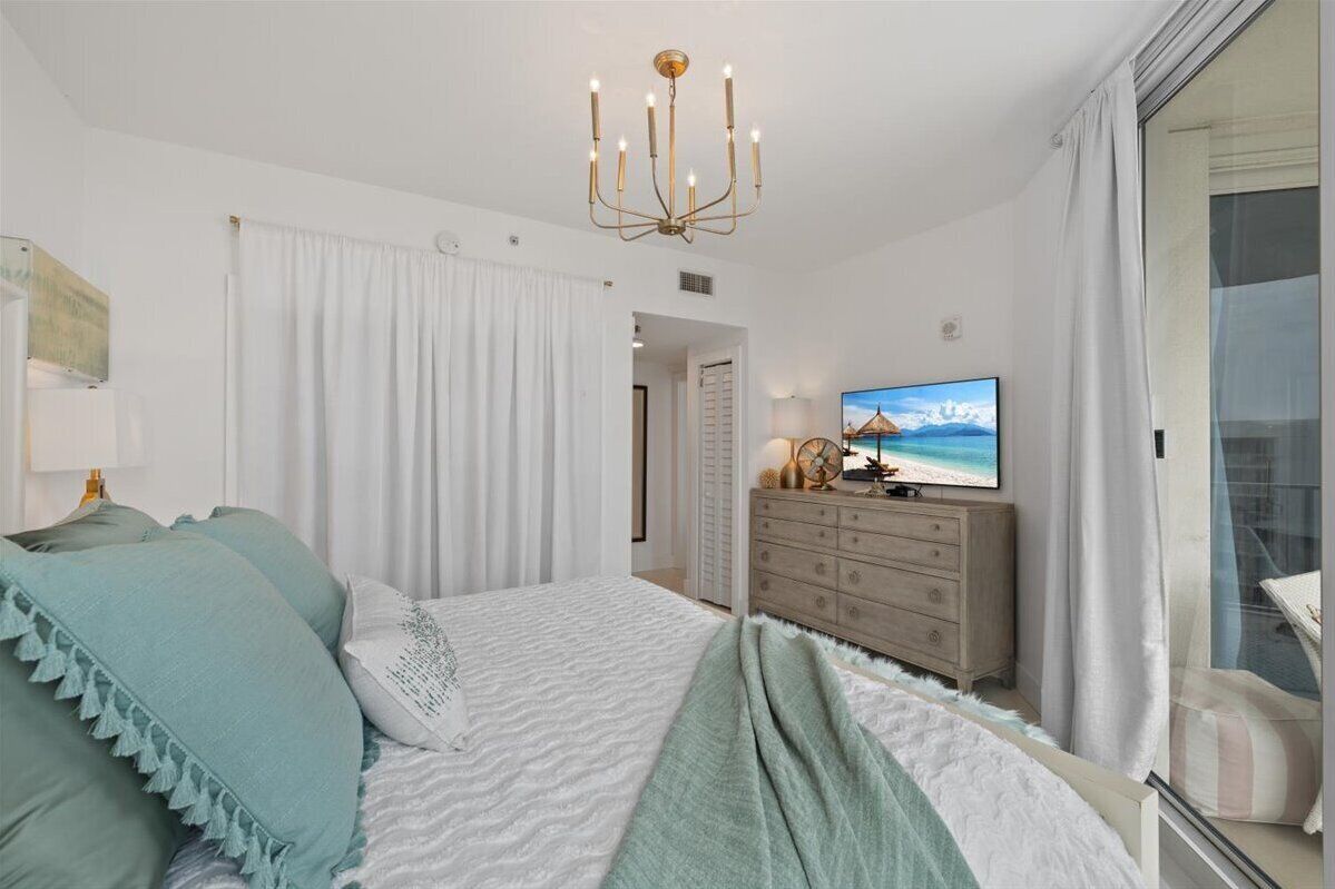 Ein Schlafzimmer mit Bett, Schminktisch, Fernseher und Meerblick durch ein Fenster.