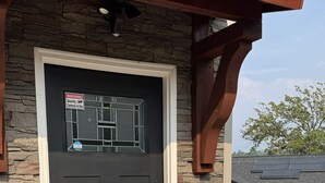 A black front door with a security camera warning sign, a metal handle, and a potted plant with red flowers.