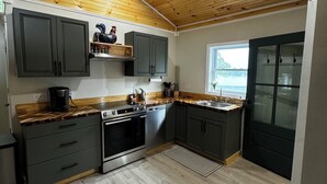 A modern kitchen with wooden ceiling, built-in cabinets, stainless steel appliances, and a window providing natural light.