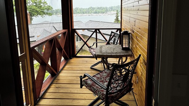 A wooden deck with a table and chairs, a lantern, and a view of a body of water and buildings.