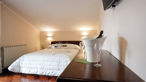 A hotel room with a neatly made bed, a bedside table with a bottle and glasses, and a wall-mounted TV. - B&B La Piazzetta (Pianillo)
