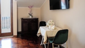 A dining area with a wooden herringbone floor, a dark wooden cabinet, a table with a white tablecloth, a green chair, and a flat-screen TV mounted on the wall. - B&B La Piazzetta (Pianillo)