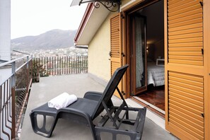 A balcony with a lounge chair and a towel, a wooden door, and a view of a city and mountains in the background. - B&B La Piazzetta (Pianillo)