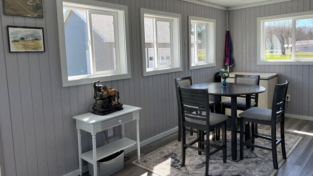 Een eetgedeelte met een ronde tafel, stoelen, een klein wit bijzettafeltje en een vloerkleed.