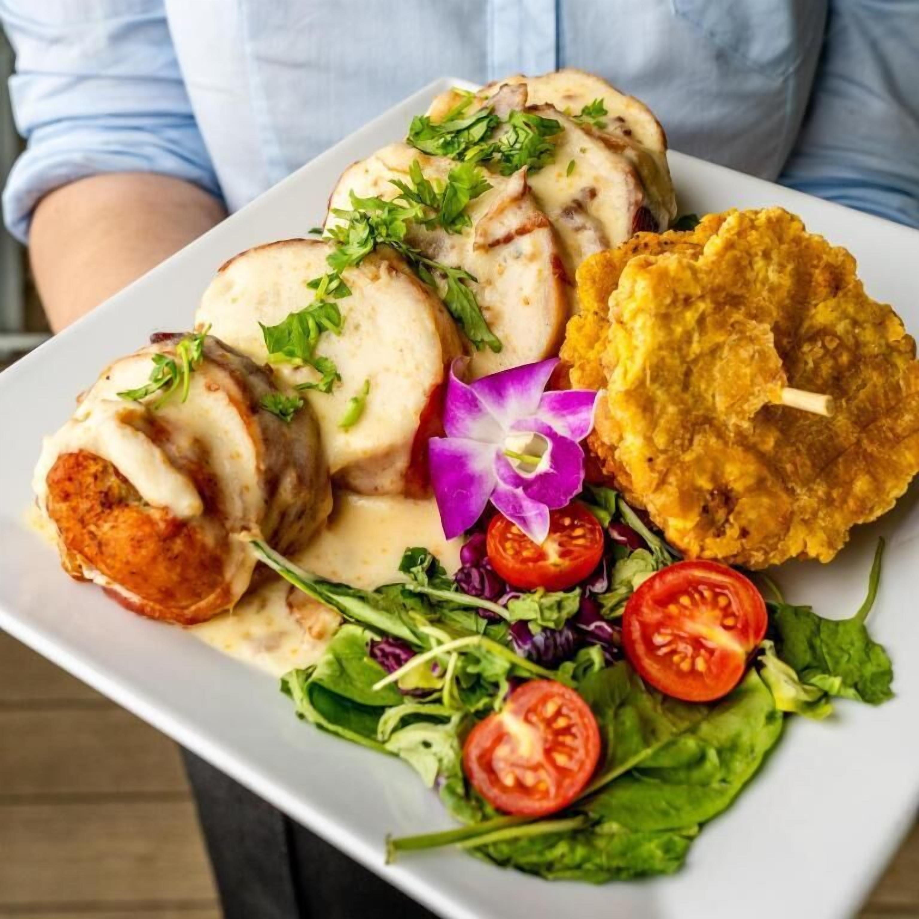 Un plato con carne en rodajas, algo frito y una ensalada de tomates y hojas verdes.