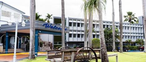 A building with a 'Welcome' sign, palm trees, and a wooden cart.