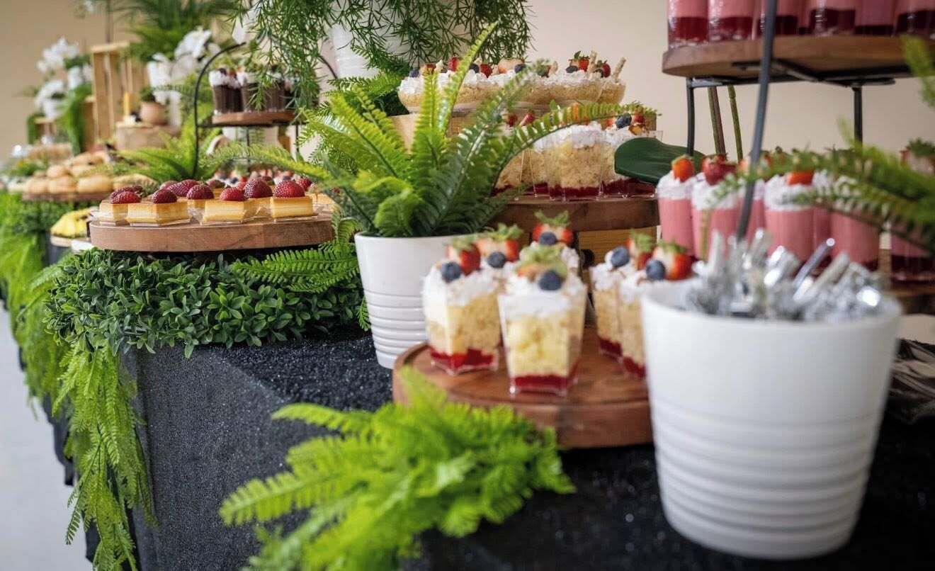 En buffé med olika sorters desserter och frukter, presenterade på träbrickor och i vita skålar.