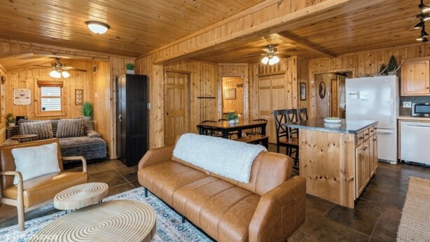 A wooden cabin interior with a living room, dining area, and kitchen.