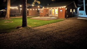 A wooden cabin with a porch, string lights, and a lawn.